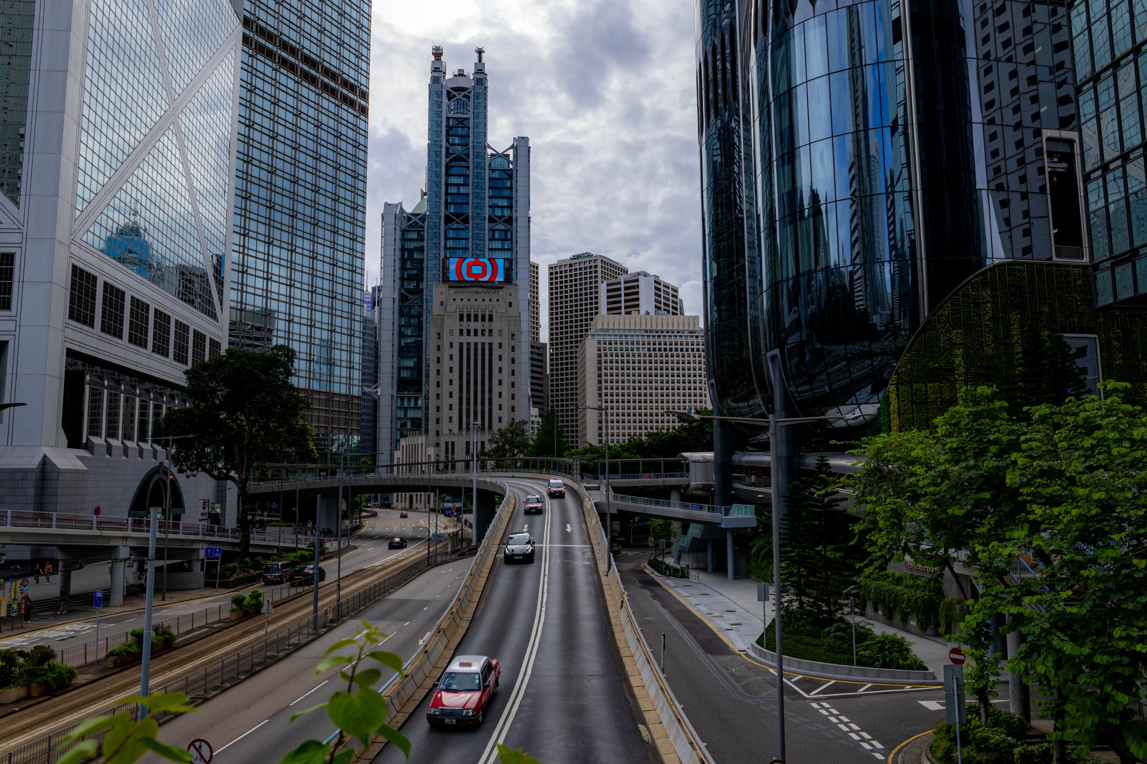 A red taxi climbing a road between Central's glass towers and footbridges, the Bank of China Tower on the left.
